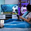 A couple is sitting on the floor in front of a TV, watching a soccer game. The TV screen displays a soccer game with a DAZN logo. There are also overlays indicating Google Home compatibility and voice control. Produktbild-Vorschau