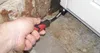 A hand is using a tool to adjust a door frame. Produktbild-Vorschau