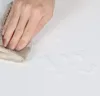 A hand is wiping a white surface with a cloth, with water droplets scattered on the surface. Produktbild-Vorschau