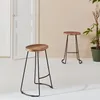 Two bar stools with wooden seats and black metal legs are shown in a room with a white door and a plant in the background. Anteprima dell’immagine prodotto