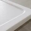 A close-up view of a white shower tray with a textured surface and a raised edge, resting on a grey tiled floor. Anteprima dell’immagine prodotto