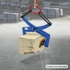 A blue stone lifting clamp is holding a light-colored stone block, suspended by a red and orange hook. The background shows a construction site with stacked materials. Náhled obrázku produktu