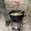 A person is cooking outdoors over a rocket stove with a cast iron pot. Produktbild-Vorschau