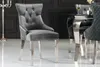 A gray velvet dining chair with silver legs and decorative studs is shown in a formal dining room setting. Produktbild-Vorschau