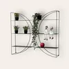 A black metal butterfly-shaped wall shelf with plants, figurines, and an apple on it. Produktbild-Vorschau