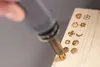A hand is using a wood burning tool to create designs on a piece of wood. Náhled obrázku produktu