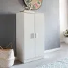 A white two-door cabinet stands against a gray wall, with a woven basket to its left and a large clock on the wall above. Produktbild-Vorschau