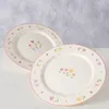 Two plates with floral patterns are displayed on a white surface against a textured gray background. Produktbild-Vorschau