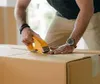 A person is taping a cardboard box closed. Produktbild-Vorschau