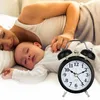 A mother and baby sleeping in bed with an alarm clock in the foreground. Voir les images du produit