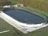 An oval swimming pool with a green cover, surrounded by grass and a hedge. Produktbild-Vorschau