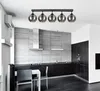 A modern kitchen with a sleek design, featuring dark cabinets, a stainless steel range hood, and a tiled backsplash. A dining table with chairs is set in the foreground, and a multi-bulb pendant light hangs from the ceiling. Náhled obrázku produktu