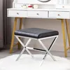 A black upholstered stool with a silver metal frame sits on a white rug in front of a white vanity table. Náhled obrázku produktu
