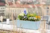 A planter box filled with spring flowers on a balcony or rooftop with a city view in the background. Náhled obrázku produktu