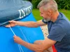 A man is kneeling and securing a blue pool cover with white ropes. Produktbild-Vorschau