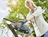A woman is using a cordless chainsaw to cut a branch outdoors. Produktbild-Vorschau