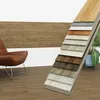 A collection of vinyl flooring samples displayed in front of a chair and a wall panel. Produktbild-Vorschau
