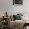A bedside table with a lamp and books next to a bed with pillows and a blanket. Produktbild-Vorschau