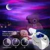 A child sleeping in bed with a teddy bear, illuminated by a star projector lamp. Produktbild-Vorschau