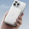 A hand holds a white power bank attached to the back of a silver smartphone against a light blue sky background. Náhľad obrázku produktu