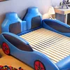 A child's bed designed to look like a race car, shown in a bedroom setting with a desk and toy blocks. Anteprima dell’immagine prodotto