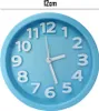 A close-up shot of a light blue analog alarm clock with white numbers and hands, set against a white background. Text indicating '12cm' is present above the clock. Produktbild-Vorschau