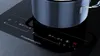 A close-up shot of a modern induction cooktop with a pot on it. Produktbild-Vorschau
