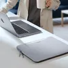 A person holding a mug stands near a laptop and a laptop sleeve on a white table. Náhľad obrázku produktu