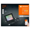 A product advertisement for a LED floodlight, showing the floodlight, a remote control, and a smartphone displaying app controls. Produktbild-Vorschau
