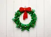 A LEGO wreath with a red bow hangs on a white wooden wall. Podgląd zdjęcia produktu