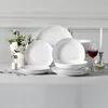 A white porcelain dinnerware set is arranged on a light gray tablecloth, with a vase of flowers and a glass of red wine. Produktbild-Vorschau