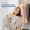 A woman is holding a coat on a hanger in front of a rack of clothes. Produktbild-Vorschau