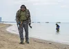 Two people metal detecting on a beach with the ocean in the background. Produktbild-Vorschau