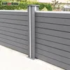A close-up view of a modern gray fence post with white accents, set against a background of green foliage and a hint of a building. Produktbild-Vorschau