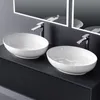 Two white ceramic washbasins on a dark vanity with illuminated mirrors in the background. Produktbild-Vorschau