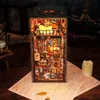A miniature diorama of a magical library or study, illuminated by warm lights, placed on a surface with old papers and a candle. Voir les images du produit