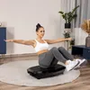 A woman is exercising on a vibration plate in a living room. Voir les images du produit