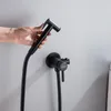 A hand holding a black bidet sprayer attached to a black hose, with a black bidet faucet mounted on a light gray wall. Podgląd zdjęcia produktu