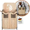 A wooden hobby horse stall with double doors and a horse head silhouette on the back panel. A smaller inset image shows two stuffed hobby horses inside a similar stall. A tag with the German flag and text is attached. Anteprima dell’immagine prodotto