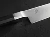 A close-up shot of a knife blade and handle against a dark, textured surface. Produktbild-Vorschau