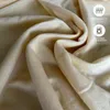 A close-up view of soft, beige-colored fabric, likely a bedsheet, with some folds and creases. There are two informational icons with text in the upper right corner. Produktbild-Vorschau