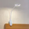 A white LED clip-on lamp with a flexible gooseneck is attached to the top edge of a wooden headboard, illuminating a textured wall. Produktbild-Vorschau