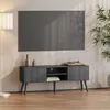 A dark gray TV stand with a TV mounted above it, in a living room setting with a plant and a lamp. Anteprima dell’immagine prodotto