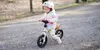 A young child is riding a balance bike on a gravel path in a park. Náhled obrázku produktu