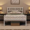 A white metal bed frame with a headboard and footboard, set up in a bedroom with nightstands and lamps on either side. A woven storage basket is placed underneath the bed. Podgląd zdjęcia produktu