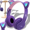 A pair of purple headphones with cat ears and LED lights is displayed on a wooden stand. Náhľad obrázku produktu