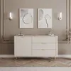 A modern beige dresser with gold accents is displayed in a well-decorated room, featuring abstract art and wall sconces. Produktbild-Vorschau