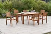A wooden garden table and chairs set on a patio, with lush greenery and flowers in the background. Produktbild-Vorschau