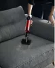 A person is using a red and silver handheld vacuum cleaner to clean a gray fabric sofa. Produktbild-Vorschau