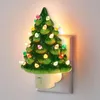 A ceramic Christmas tree night light plugged into a wall outlet. Náhľad obrázku produktu